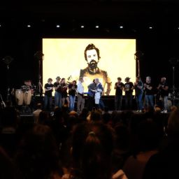 Imagen concierto jarabe de palo homenaje a Pau Donés siluetas de artistas en el escenario con una imagen de Pau Donés en pantalla