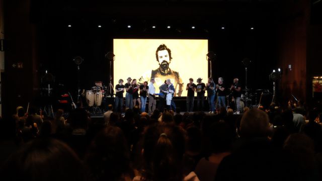 Imagen concierto jarabe de palo homenaje a Pau Donés siluetas de artistas en el escenario con una imagen de Pau Donés en pantalla