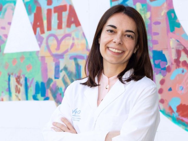 La Dra, Eva Muñoz Cosuelo con bata VHIO en una pared con letras de colores